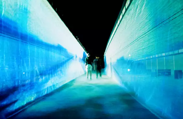54: Manchester's installation in the Warehouse. It shows two people walking through a fabric walkway, which is illuminated by blue lights.