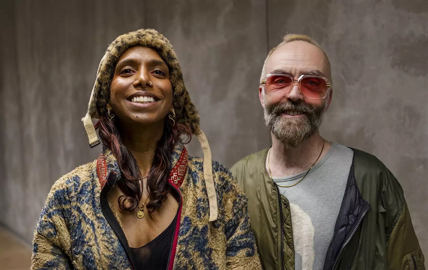 Photo of (left) Myra Appannah and (right) Simon Wilkinson – of BRiGHTBLACK – smiling. Myra is wearing a fluffy leopard-print hat. Simon is wearing rose-tinted glasses.
