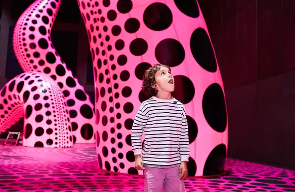 A child stands in a Yayoi Kusama exhibition with pink and black tentacles