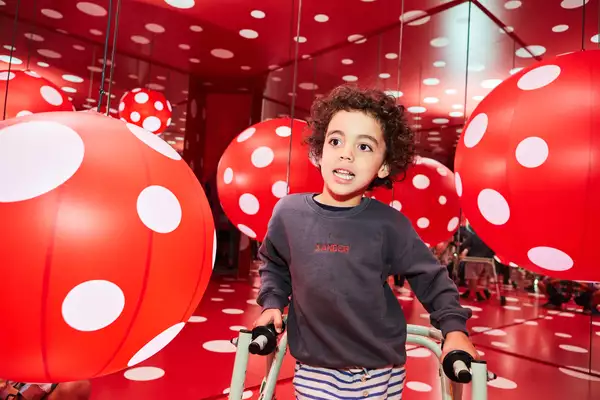 A child plays in a red and white polka dot patterned room by Yayoi Kusama