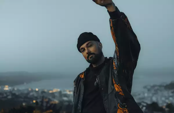 Photo of Rei with his arm in the air wearing a black hat and jacket