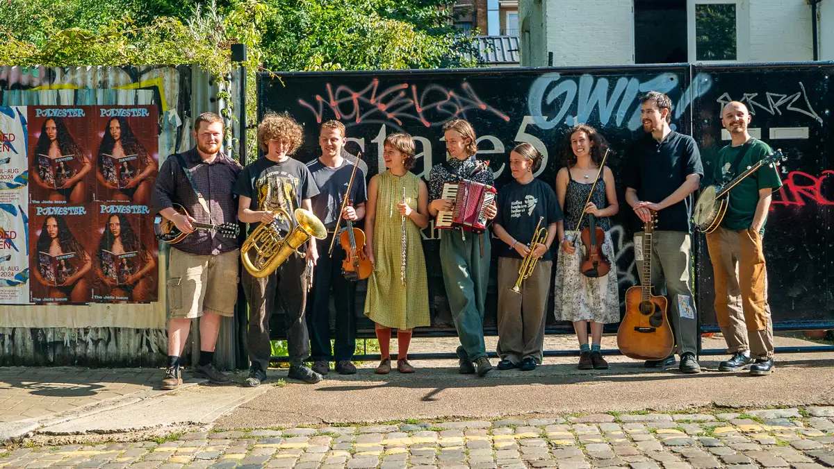 Photo of 9 members of Brown Wimpenny stood outside on a cobbled street with their instruments