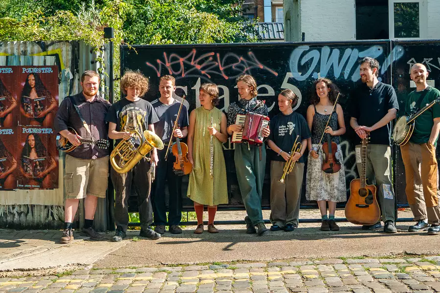 Photo of 9 members of Brown Wimpenny stood outside on a cobbled street with their instruments