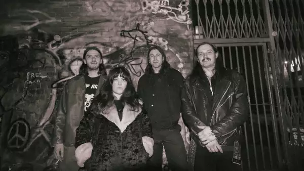 Grainy sepia photo of four members of Deaf Whip stood outside by a wall covered in graffiti
