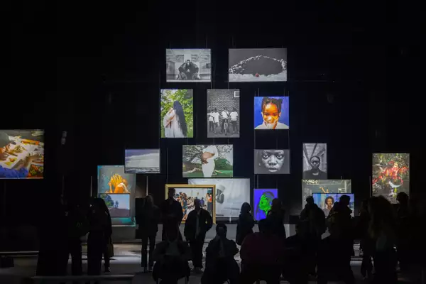 A group of people stood in the Reframe exhibition looking at the photographs, which are hanging from the ceiling of the Warehouse
