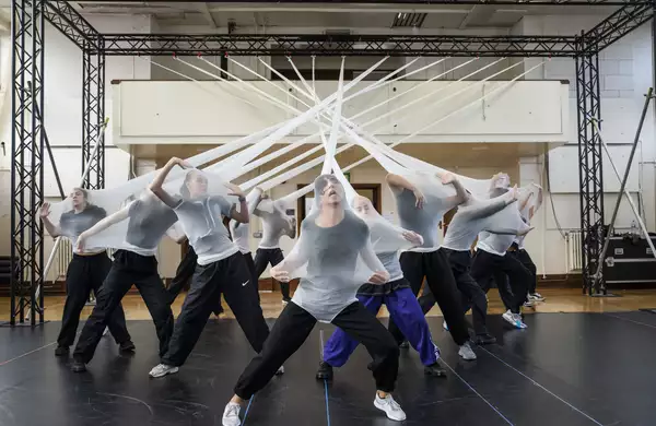 Dancers in stretched white fabric attached to a rig in rehearsals for Free Your Mind