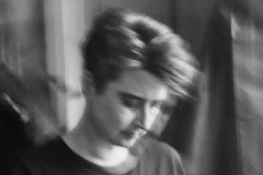 A black and white photo of Ghost Assembly with short, tousled hair, looking down. The image is intentionally blurred, creating a soft, dreamlike effect.