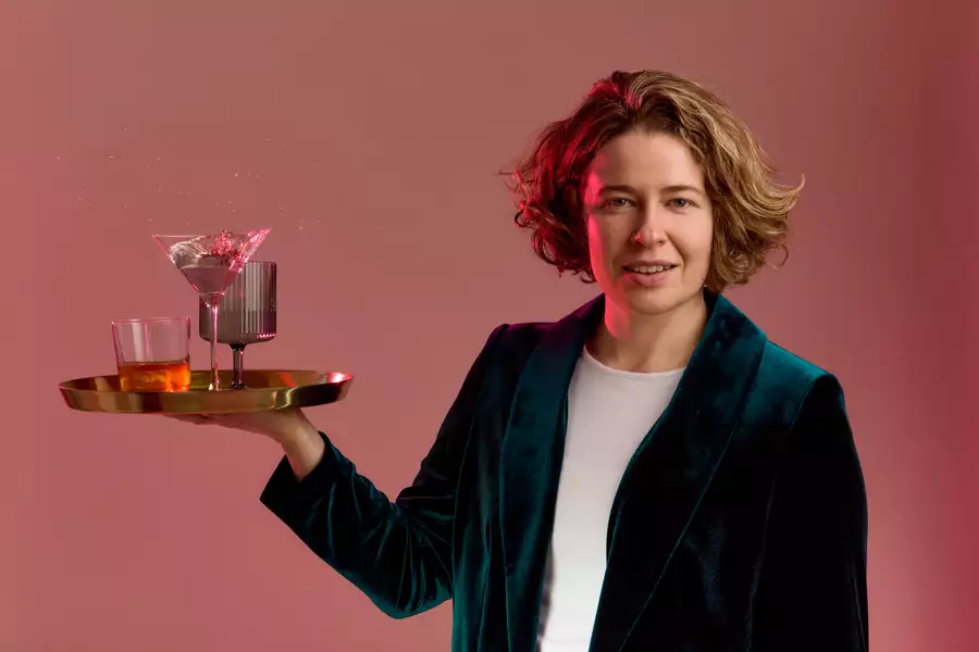 Holly Redford Jones looks into the camera holding a tray of cocktails in a velvet green suit jacket.