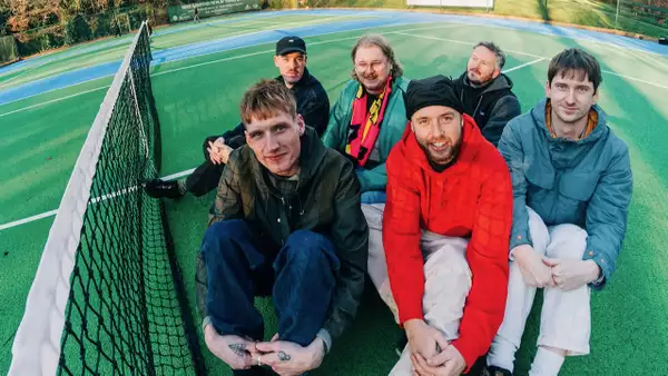 Six members of Adult DVD sat on the floor of a a tennis court next to the net