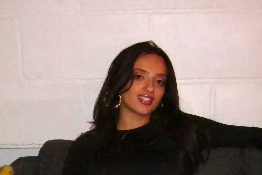 SOPHIA sat on a sofa in front of a white wall, smiling and wearing a long-sleeved black top