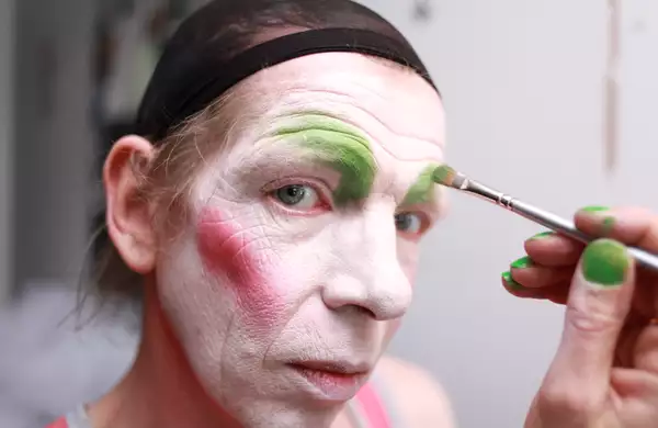 Close-up photo of David Hoyle having his face painted, looking at the camera