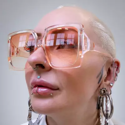 Headshot of Loll looking to the side, wearing big pink sunglasses and silver earrings