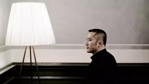 Huang Ruo looking to the side, posing next to a large white lamp