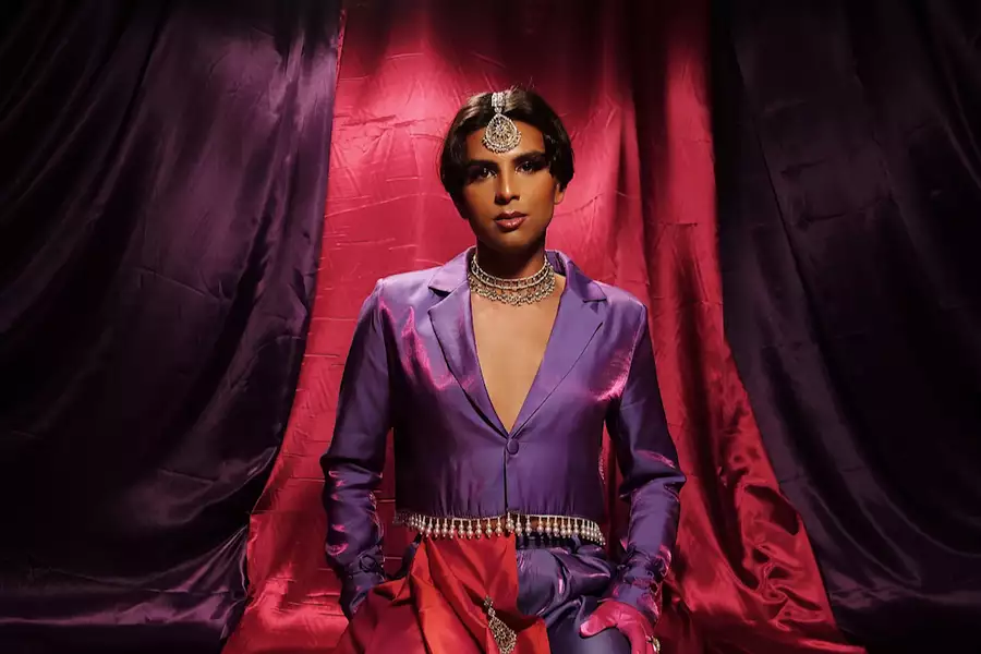 Jason Patel wears a purple and pink suit, against a backdrop of deep purple and pink draped fabric, looking confidently at the camera.
