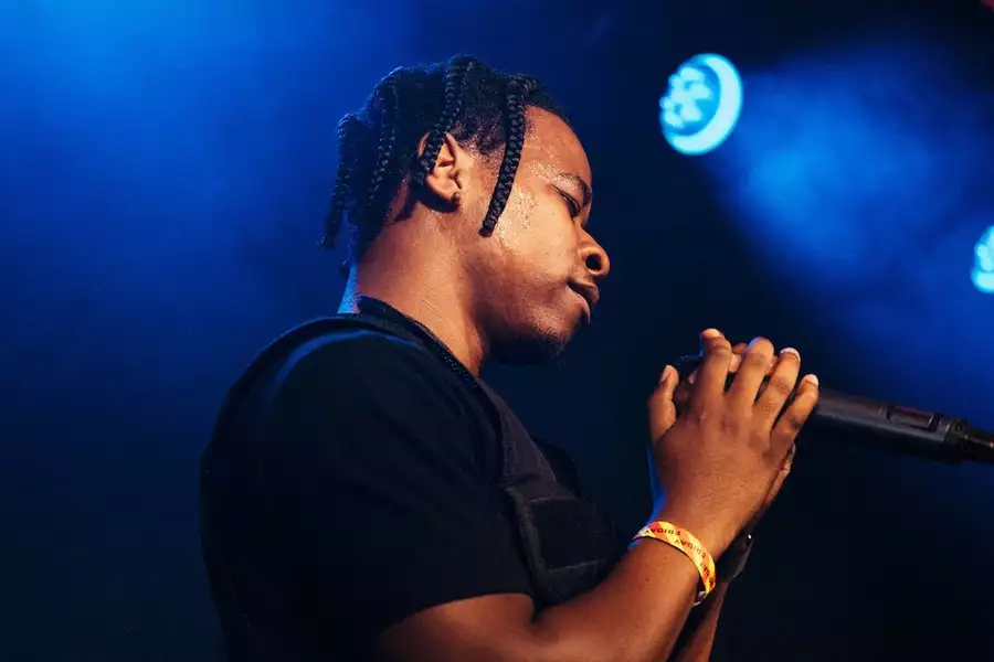 PRIDO singing into a microphone on Festival Square. The lighting is blue.
