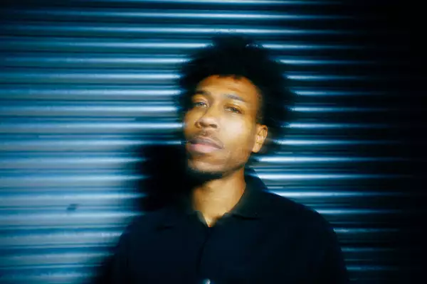 Obeka looking towards the camera. He is stood against a shutter.