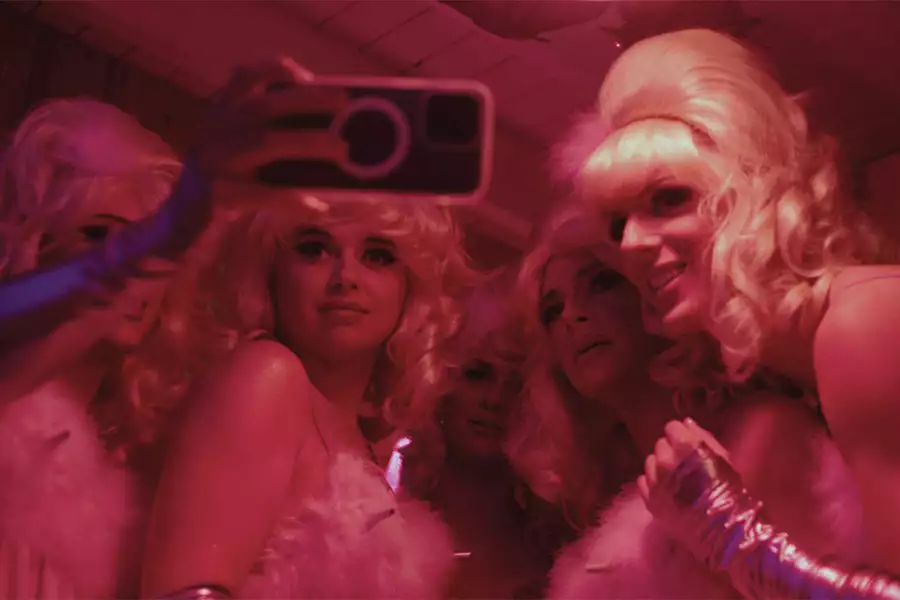 A still from A House Is Not A Disco, showing a group of people dressed up and taking a selfie. The image has a pink hue.