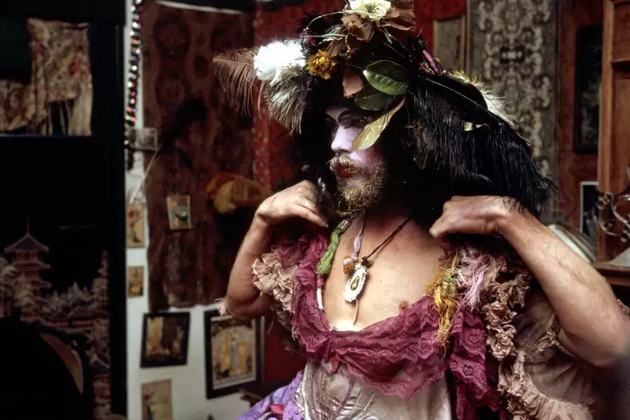 A still from David Weissman's documentary The Cockettes. It shows a person dressed up in a pink ballgown with a headdress made of flowers and feathers.