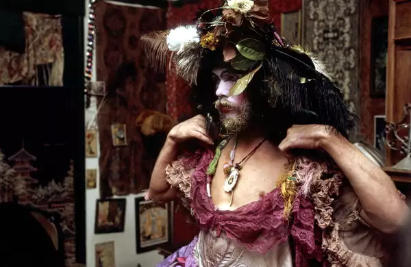 A still from David Weissman's documentary The Cockettes. It shows a person dressed up in a pink ballgown with a headdress made of flowers and feathers.