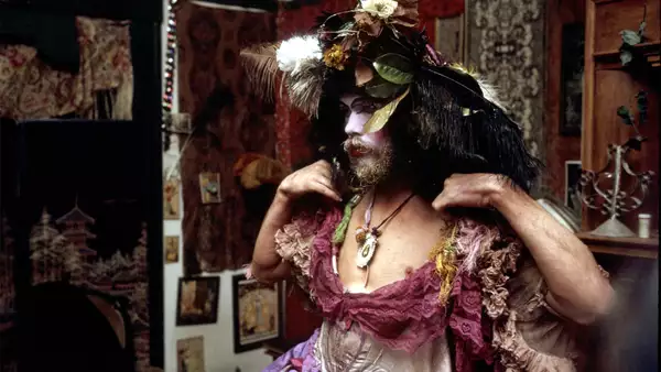 A still from David Weissman's documentary The Cockettes. It shows a person dressed up in a pink ballgown with a headdress made of flowers and feathers.