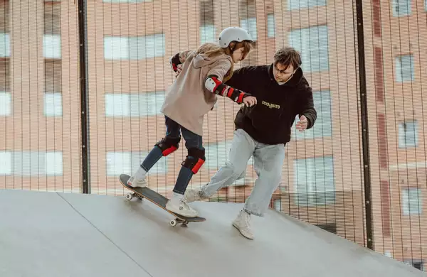 Photo of an instructor teaching a young person to skateboard on a ramp