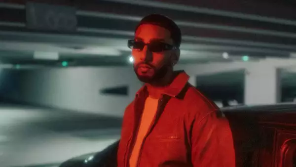 Blurred photo of Sagan stood in an underground car park wearing dark shades.