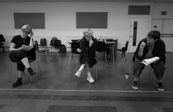 Black and white photograph of three people sat on a chair during THEY rehearsals