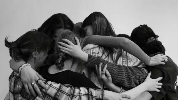A black and white photograph of young people with their arms around each other in a group cuddle