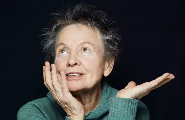 A photograph of artist Laurie Anderson seated in a green jumper