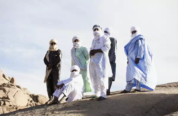 Members of Tinariwen stood on a large rock in the sunshine