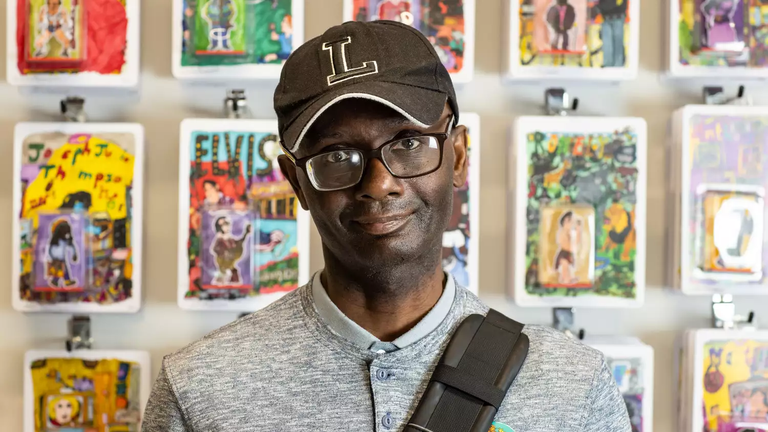 Leslie Thompson wearing a black cap with an 'L' on, stood in front of a wall of artwork