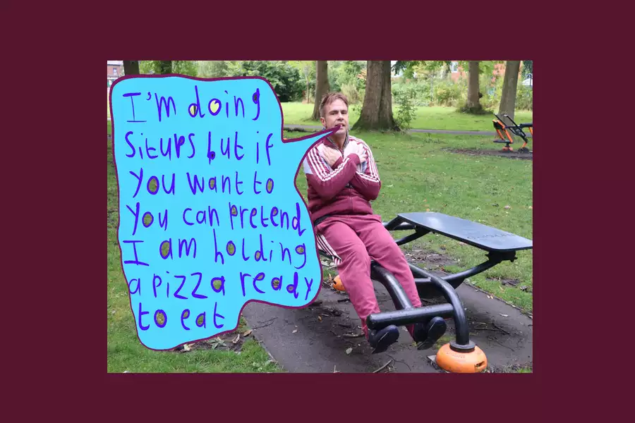 Photo of Liam Ashworth sat on an exercise bench in a park. There is a blue drawn speech bubble overlayed on the image, which says ‘I’m doing situps but if you want to you can pretend I am holding a pizza ready to eat’