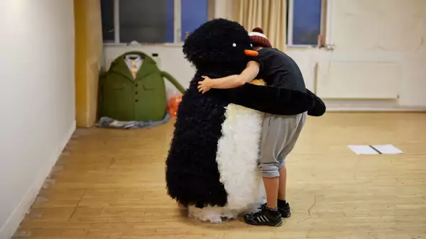 A puppet penguin and actor share a hug in Lost and Found rehearsals