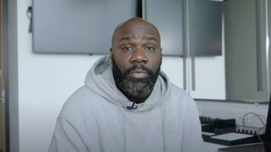 Michael 'Mikey J' Asante sits in at a desk wearing a grey hoodie