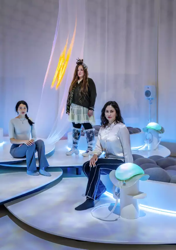 Photo of three women in a white room in front of a white curtain